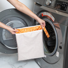 Load image into Gallery viewer, A person holds a Bumkins Wet/Dry Bag: Grounded in front of an open front-loading washing machine.
