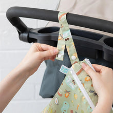 Load image into Gallery viewer, A person attaching a Bumkins Wet/Dry Bag: Camp Gear, crafted from waterproof fabric, to a stroller handle using a snap button strap.
