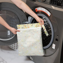 Load image into Gallery viewer, A person holds Bumkins Wet/Dry Bag: Camp Gear in front of an open front-loading washing machine.
