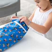 Load image into Gallery viewer, A child in a white dress opens a blue Bumkins Wet/Dry Bag: Mickey &amp; Friends Forever while sitting at a white table.
