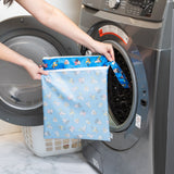 A person holds Bumkins Wet/Dry Bag: Mickey & Friends Forever in front of an open front-loading washing machine.