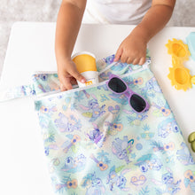 Load image into Gallery viewer, A child puts sunscreen and sunglasses in a colorful Bumkins Wet/Dry Bag: Aloha Stitch on a white table.
