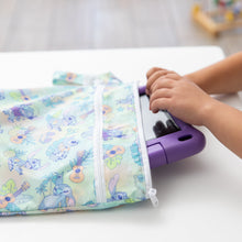 Load image into Gallery viewer, A child places a purple tablet in a colorful Bumkins Wet/Dry Bag: Aloha Stitch on a white table.
