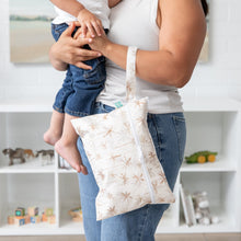 Load image into Gallery viewer, Close-up of a person holding a child and a Bumkins Wet/Dry Clutch: Palm Daze on their arm, standing in a room with a bookshelf.
