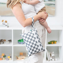 Load image into Gallery viewer, A woman holds a child and a Bumkins Wet/Dry Clutch: Charcoal Check in a toy-filled room.
