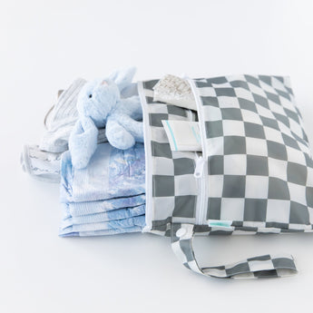 Bumkins Wet/Dry Clutch: Charcoal Check is unzipped to reveal folded clothes and a blue plush bunny on a white backdrop.