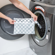 Load image into Gallery viewer, A person holds a Bumkins Wet/Dry Clutch: Charcoal Check by an open washing machine.
