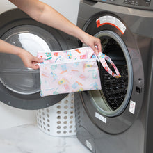 Load image into Gallery viewer, A person holds a Bumkins Wet/Dry Clutch: Boots in front of a front-loading washing machine.
