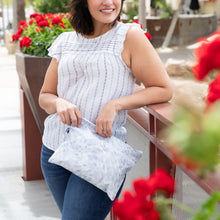 Load image into Gallery viewer, A woman in a striped blouse holds a Roamio by Bumkins Wet/Dry Clutch: Disco Check, smiling by red flowers while leaning on a railing.
