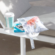 Load image into Gallery viewer, A Roamio by Bumkins Wet/Dry Clutch: Disco Check with pink sunglasses and books sits by a coffee cup on a table next to a gray cushioned chair.
