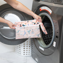 Load image into Gallery viewer, A person holds a Bumkins Wet/Dry Clutch: Yoga Pals in front of an open washing machine next to a white laundry basket.
