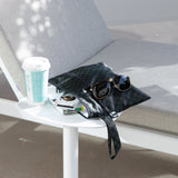 Roamio by Bumkins Wet/Dry Clutch: Rich Black sits on a table outdoors next to a lounge chair with sunglasses, books, and a coffee cup.