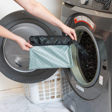 Load image into Gallery viewer, A person holds Roamio by Bumkins Wet/Dry Clutch: Rich Black in front of an open front-loading washing machine.
