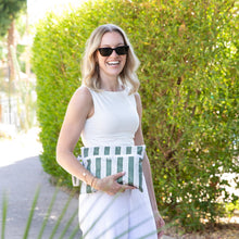 Load image into Gallery viewer, A smiling woman in a white outfit with sunglasses holds a Roamio by Bumkins Wet/Dry Clutch: Clubhouse Stripe by greenery outdoors.
