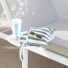 Load image into Gallery viewer, Roamio by Bumkins Wet/Dry Clutch: Clubhouse Stripe with sunglasses &amp; a coffee cup sits on a table in sunlight next to a gray cushioned chair.
