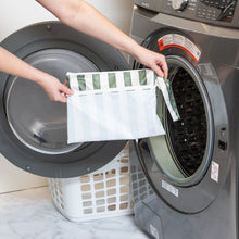 Load image into Gallery viewer, A person holds Roamio by Bumkins Wet/Dry Clutch: Clubhouse Stripe in front of an open front-loading washing machine.
