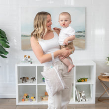 Load image into Gallery viewer, A woman smiles holding her baby in a room with white shelves and toys, carrying a Bumkins Wet/Dry Clutch: Wander.
