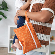 Load image into Gallery viewer, In a cozy room with a bookshelf and plant, a person cradles a baby and holds a Bumkins Wet/Dry Clutch: Grounded on their arm.
