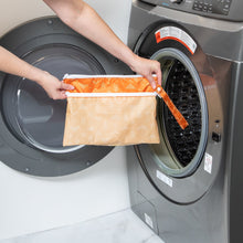 Load image into Gallery viewer, A person holds a Bumkins Wet/Dry Clutch: Grounded in front of a a front-loading washer.
