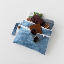 Load image into Gallery viewer, Roamio by Bumkins Wet/Dry Clutch: Crushed Denim stores sunglasses, passport, clothes, and a hair clip on a white background.
