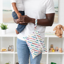 Load image into Gallery viewer, A man holds a child and a Bumkins Wet/Dry Clutch: Mickey &amp; Friends Varsity on his arm; toys and plant on shelves behind them.

