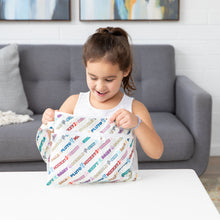 Load image into Gallery viewer, A smiling girl sits at a white table, opening a Bumkins Wet/Dry Clutch: Mickey &amp; Friends Varsity.
