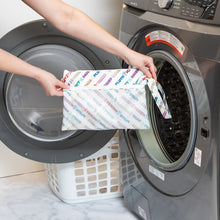 Load image into Gallery viewer, A person holds Bumkins Wet/Dry Clutch: Mickey &amp; Friends Varsity in front of an open front-loading washing machine.
