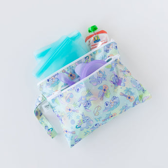 Bumkins Wet/Dry Clutch: Aloha Stitch holds turquoise bags, a purple bowl with matching spoon, and an applesauce pouch on a white background.
