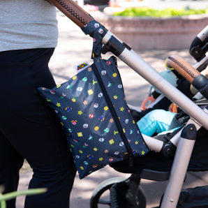 A person pushes a stroller outdoors with a Bumkins Wet/Dry Clutch: Super Mario™ Lineup attached to the handle.
