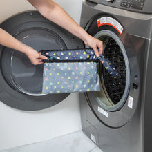 Load image into Gallery viewer, A person holds Bumkins Wet/Dry Clutch: Super Mario™ Lineup in front of an open front-loading washing machine.
