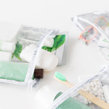 Load image into Gallery viewer, Close-up of toiletries in Roamio by Bumkins Clear Travel Bag 3 Pack: Disco Check on a white background.
