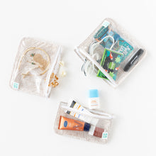 Load image into Gallery viewer, Bumkins Clear Travel Bag 3-Pack: Wander  is neatly arranged on a white background holding toiletries, hair accessories, books, &amp; goggles.
