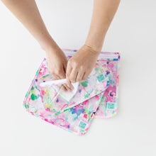 Load image into Gallery viewer, A person uses a cloth to clean the interior of Bumkins Clear Travel Bag 3-Pack: Watercolor on a white background.
