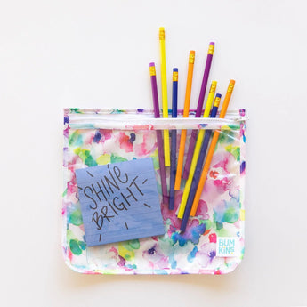 Vibrant pencils peek from a Bumkins Clear Travel Bag 3-Pack: Watercolor on a white background, with a blue note stating “Shine Bright” inside.