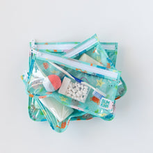 Load image into Gallery viewer, Bumkins Clear Travel Bag 3-Pack: Ocean Life lays stacked on a white background, filled with toiletries.
