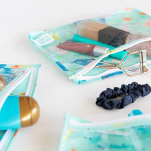 Load image into Gallery viewer, Close-up of Bumkins Clear Travel Bag 3-Pack: Ocean Life with makeup items, hair ties, and accessories on a white background.
