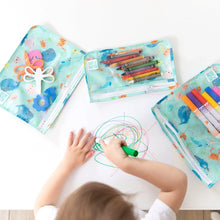 Load image into Gallery viewer, A child draws colorful scribbles with a marker on paper, with art supplies in Bumkins Clear Travel Bag 3-Pack: Ocean Life nearby.
