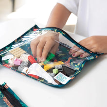 Load image into Gallery viewer, A child's hand reaches for colorful toy brick pieces from a Bumkins Clear Travel Bag 3-Pack: Jungle on a white table.
