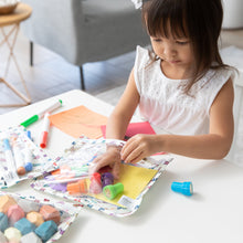 Load image into Gallery viewer, A young girl in a white dress pulls stamps out of a Bumkins Clear Travel Bag 3 Pack: Mickey &amp; Friends Varsity on a table with art supplies.
