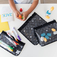 Load image into Gallery viewer, A child plays with markers, stamps, and art supplies in Bumkins Clear Travel Bag 3-Pack: Mickey Mouse Icon Black + White at a white table.
