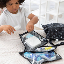 Load image into Gallery viewer, A boy packs toiletries into Bumkins Clear Travel Bag 3-Pack: Mickey Mouse Icon Black + White on a beige bedspread.
