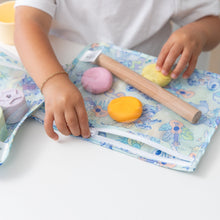 Load image into Gallery viewer, A child wearing a bracelet zips a Bumkins Clear Travel Bag 3 Pack: Aloha Stitch filled with colorful modeling clay on a white table.

