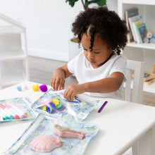 Load image into Gallery viewer, A curly-haired child at a white table reaches for art supplies stored in Bumkins Clear Travel Bag 3 Pack: Aloha Stitch.
