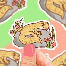 Load image into Gallery viewer, Cartoon gecko vinyl sticker by Turtle Soup: smiling yellow gecko on a rock with pink flowers, surrounded by more colorful geckos.
