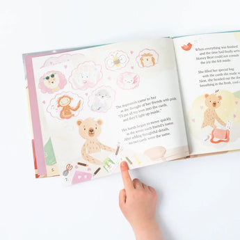 A childs hand points to Thinking of You by Slumberkins, featuring Honey Bear and animals, capturing winter gratitude.