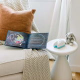 A childrens book, cozy chair, knitted blanket, brown cushion nearby with a plush rabbit and Tooth Fairy Flylight Box Set on a table.
