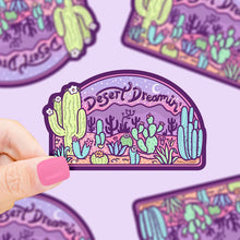 Load image into Gallery viewer, A hand holds a Turtle Soups Desert Dreaming durable waterproof vinyl sticker, featuring cacti and a desert scene under a starry sky.
