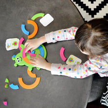 Load image into Gallery viewer, A child enjoys the Bugzzle Game by Fat Brain Toy Co, placing colorful pieces on a green turtle, with matching symbol cards scattered around.
