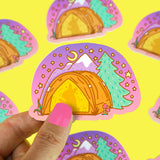 A hand holds Turtle Soups Vinyl Sticker, Camping Tent, featuring a crescent moon and starry sky over a yellow tent with mountains and a pine tree. The colorful, scratch-resistant, waterproof design repeats on a bright yellow surface.