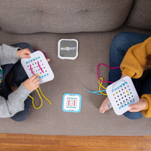 Load image into Gallery viewer, Two people sit on a gray couch, each holding a Sew Fast sewing card by Fat Brain Toy Co., a creative game challenging spatial reasoning. Colorful threads lace the cards they hold. The Sew Fast game box and another card rest between them on the wooden floor.
